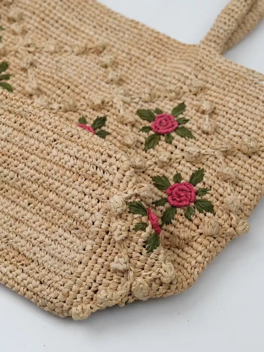 Close-up of red rose appliques and green leaves on a woven raffia tote