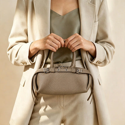 Woman in a cream suit holding the taupe leather east-west satchel