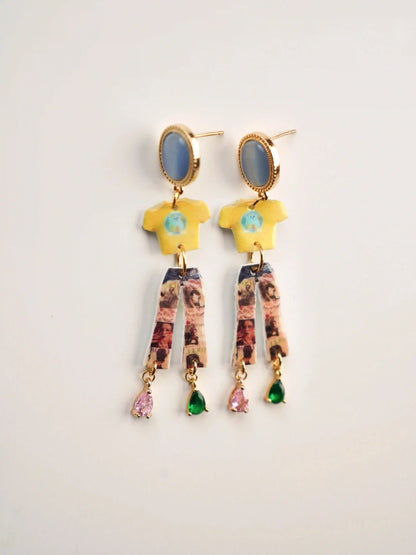 Close-up of handmade resin composite charm earrings with retro clothing motifs and mismatched crystal accents by HERIZONE