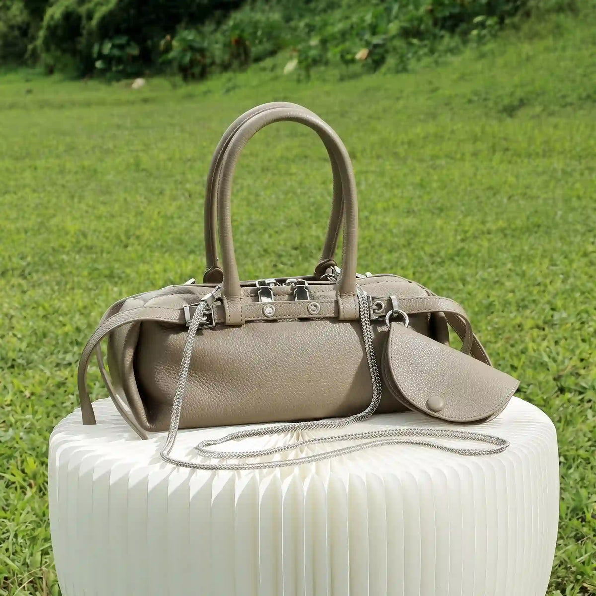 Taupe leather east-west satchel with chain strap displayed outdoors