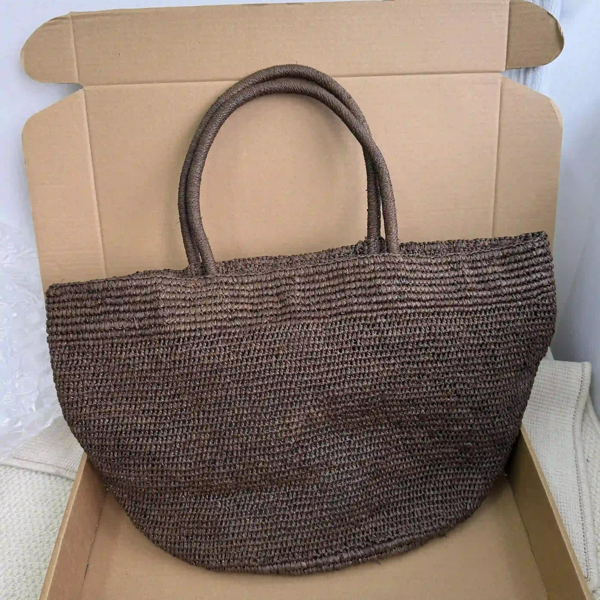 Large dark brown handwoven raffia tote with half-moon silhouette, artisan natural fiber beach bag for summer vacation