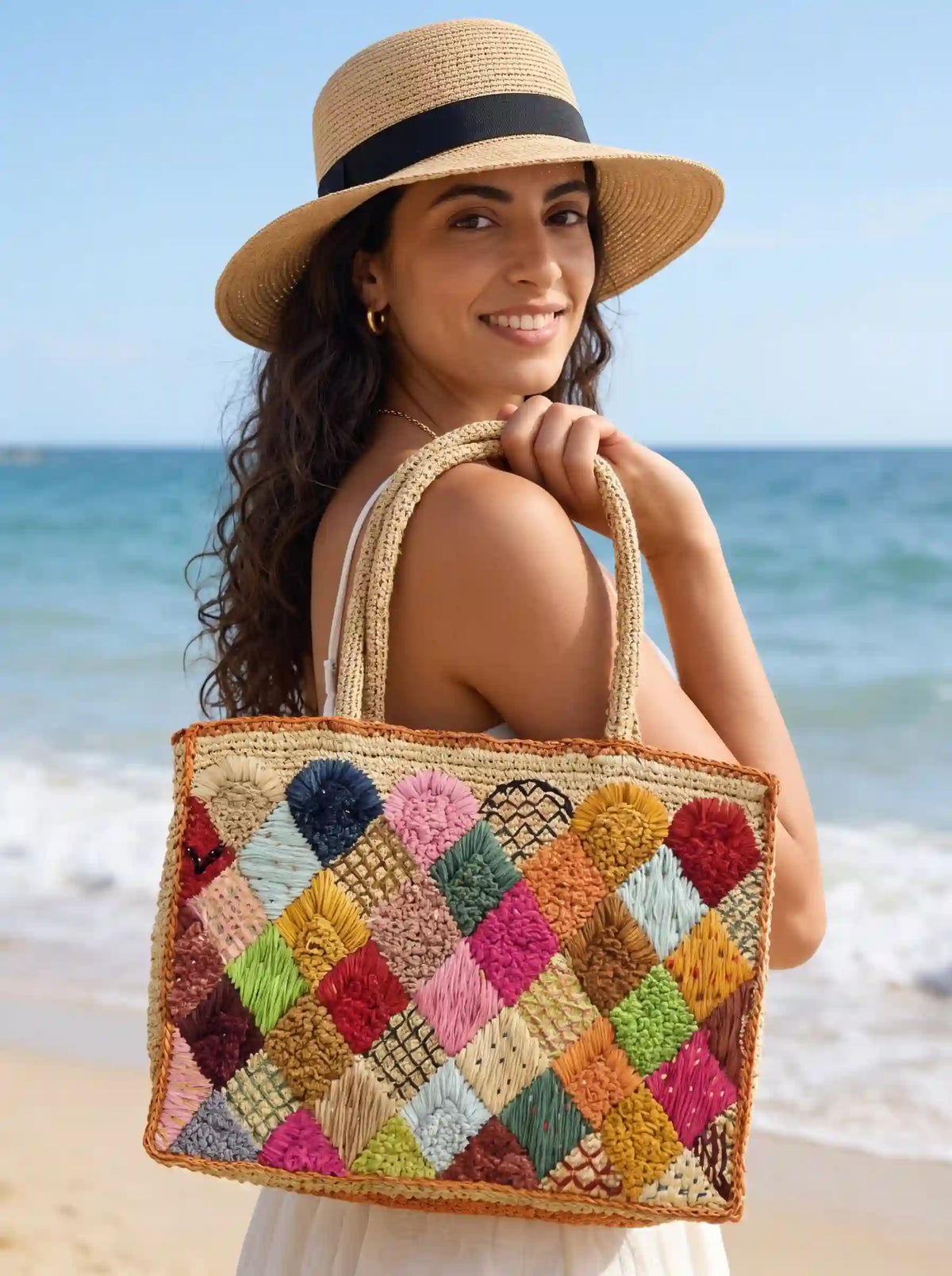 Woman carrying colorful patchwork raffia tote bag on the beach – handwoven natural fiber summer handbag – boho chic vacation style