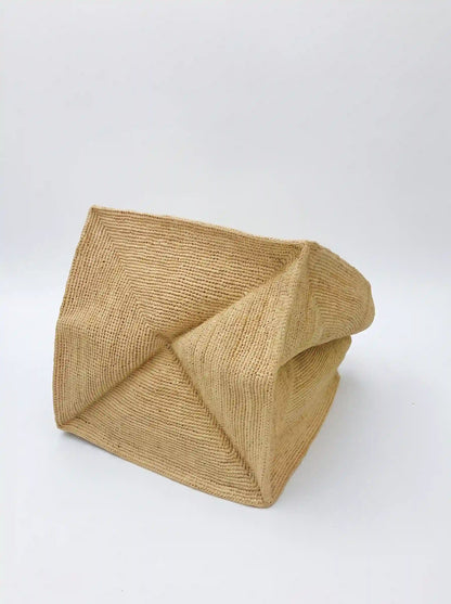 Close-up of natural raffia tote bag showing structured geometric base and tightly woven fiber texture on white background
