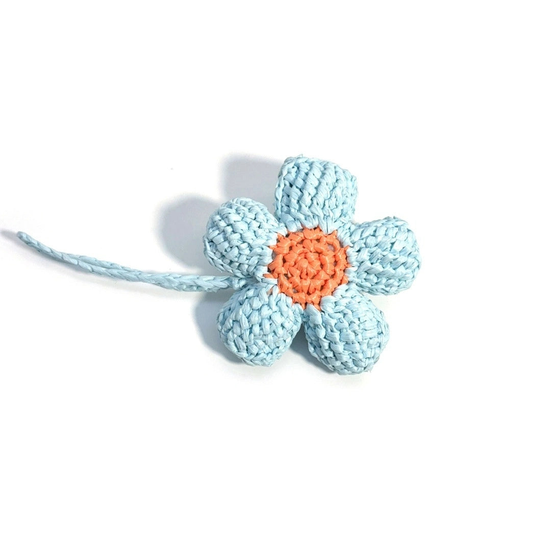 Handmade blue raffia flower bag charm laid flat, showing five sculpted petals, an orange center, and a braided hanging cord.