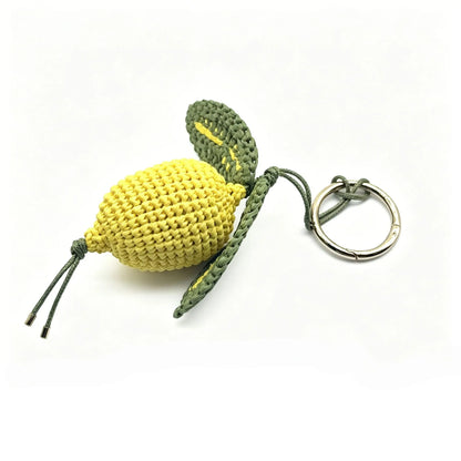 Yellow hand-crocheted raffia lemon bag charm with green leaves and a round metal clasp on a white background.