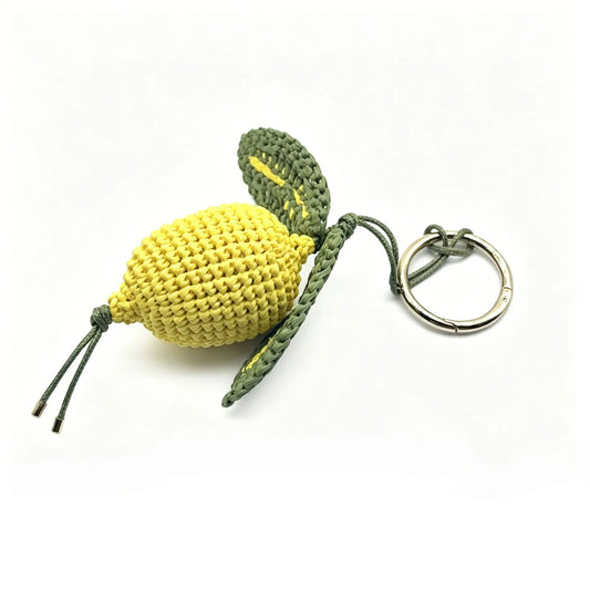 Yellow hand-crocheted raffia lemon bag charm with green leaves and a round metal clasp on a white background.