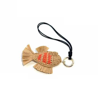 Natural raffia fish bag charm with orange stripes, fringed fins and tail, and a black hanging loop on white.