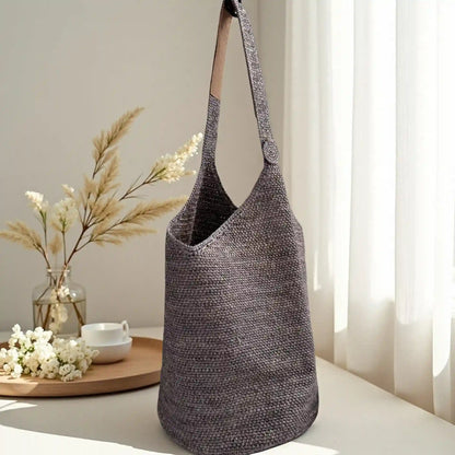 Dark grey crochet raffia bucket bag with leather shoulder strap, minimalist woven handbag styled in soft natural light home setting